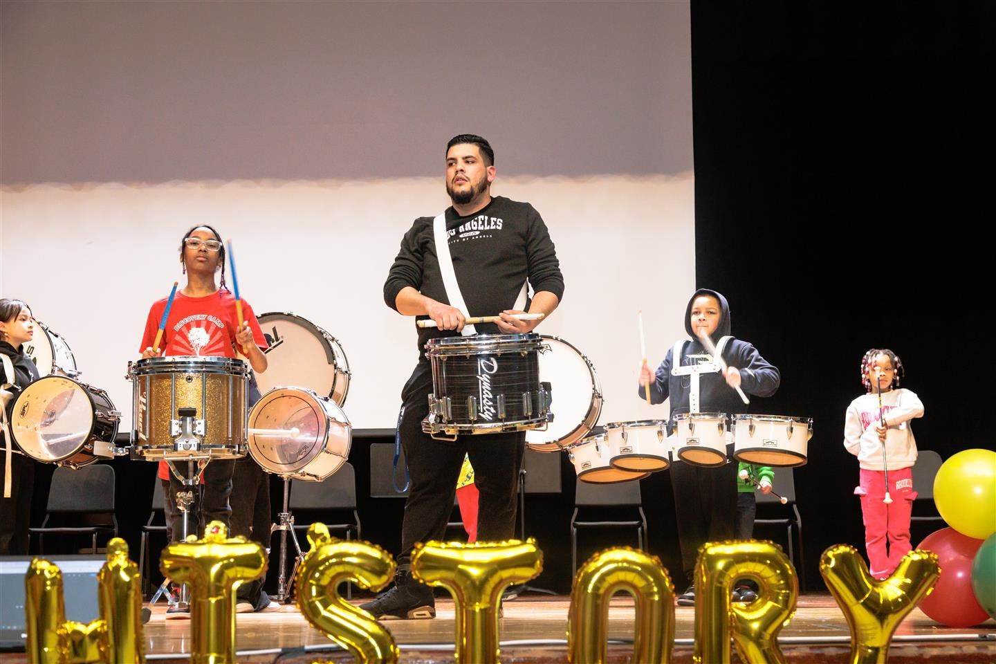 Students and an instructor perform on drums.